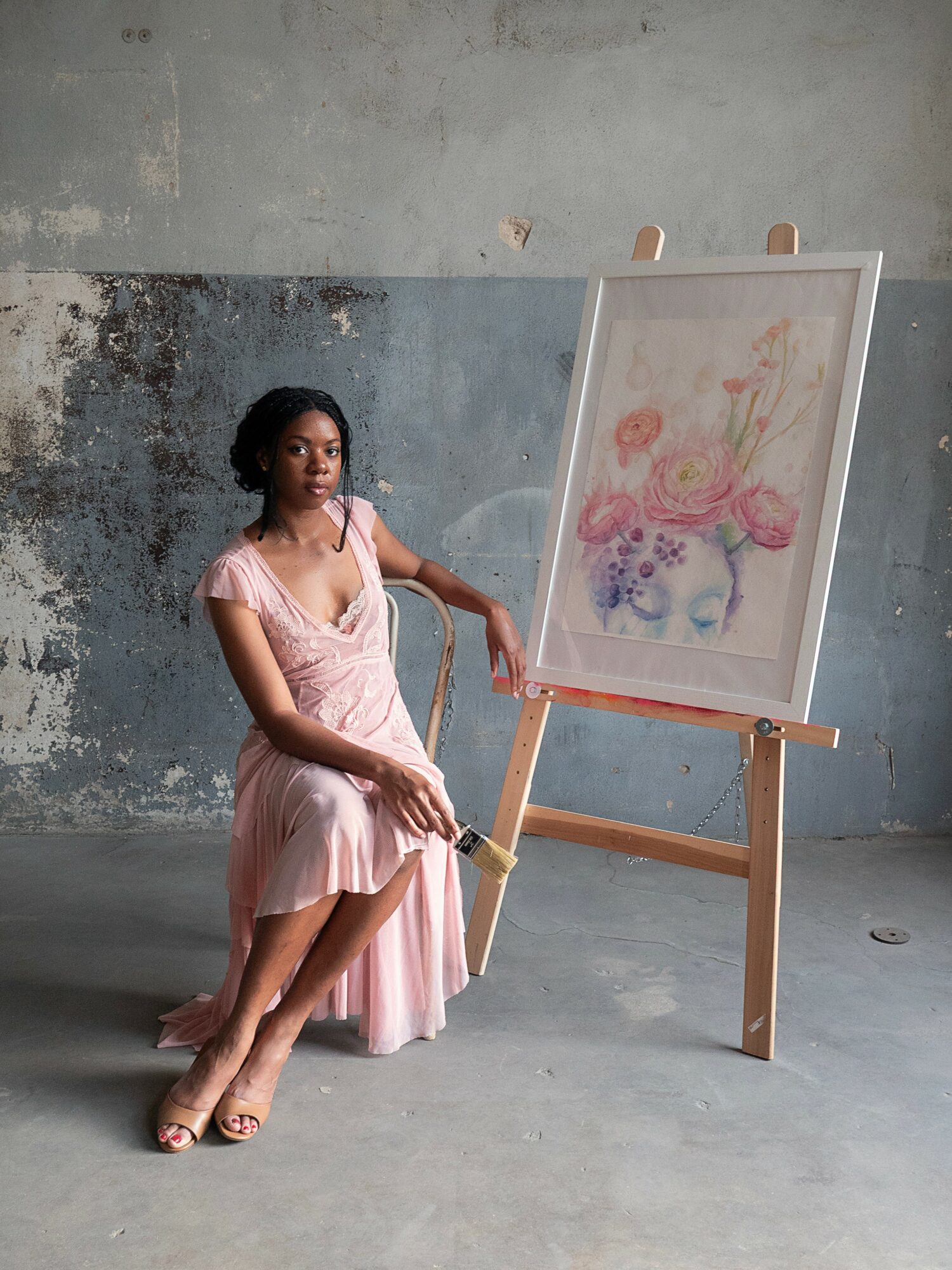 Bukola Jaji seated beside an easel with a floral watercolor painting